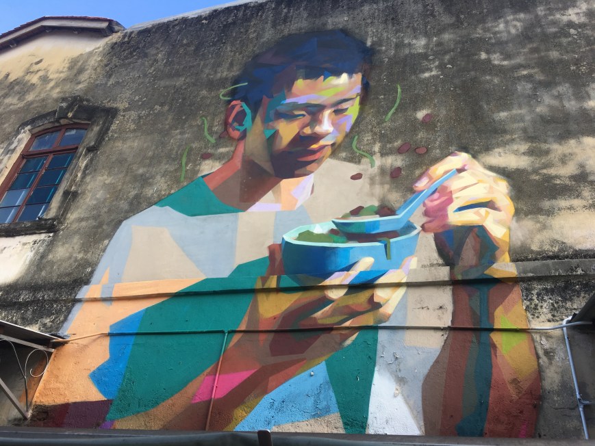Mural of a man eating chendul outside the street stall