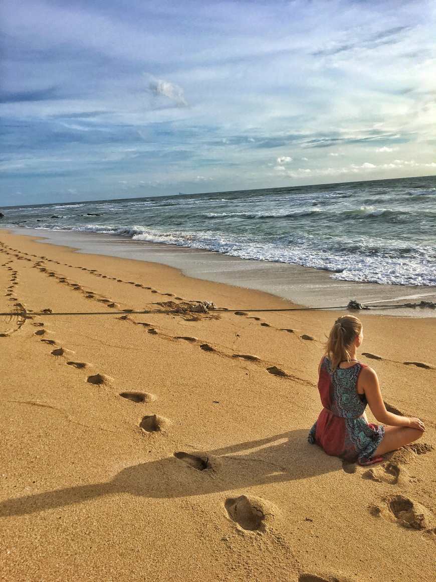 Sitting and meditation on the beach at sunset in Koh Lanta Thailand with foot prints in the sand