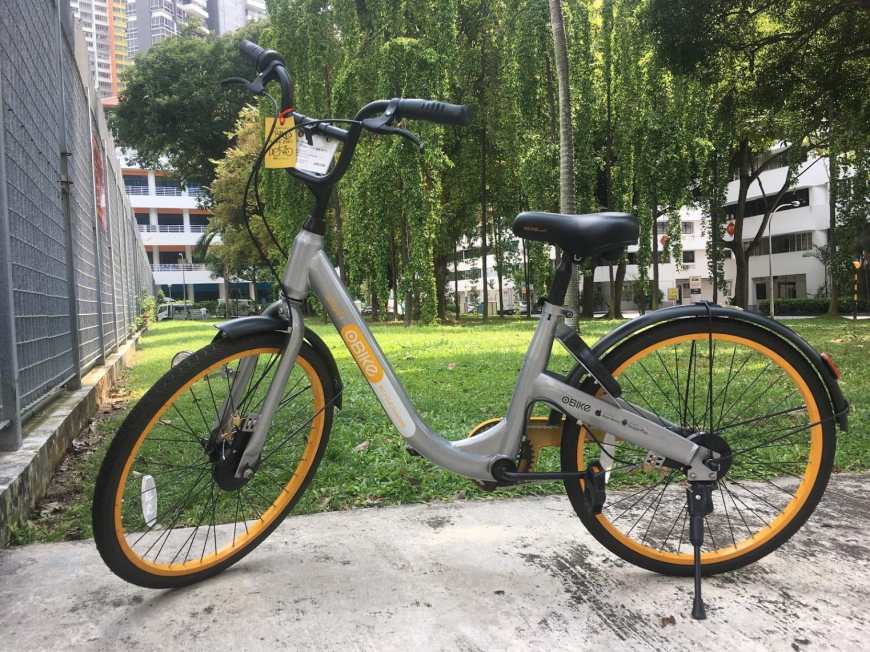 Grey bicycle with black and yellow wheels on a sidewalk in Singapore with grass behind