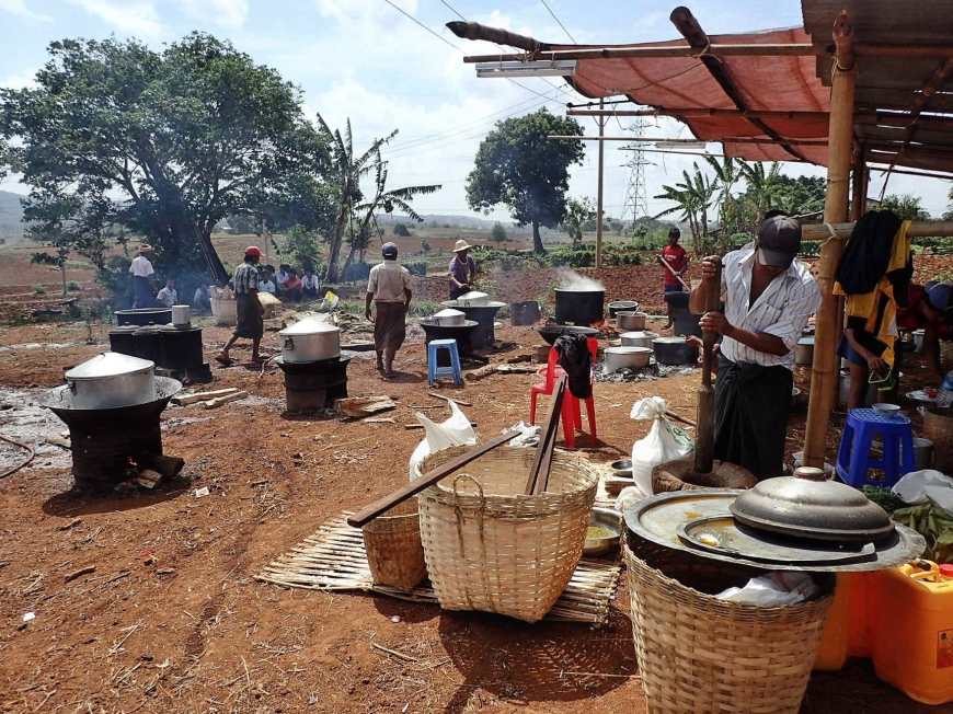 A field filled with different cooking fires covered with pots emanating steam to cook the food for a Burmese wedding
