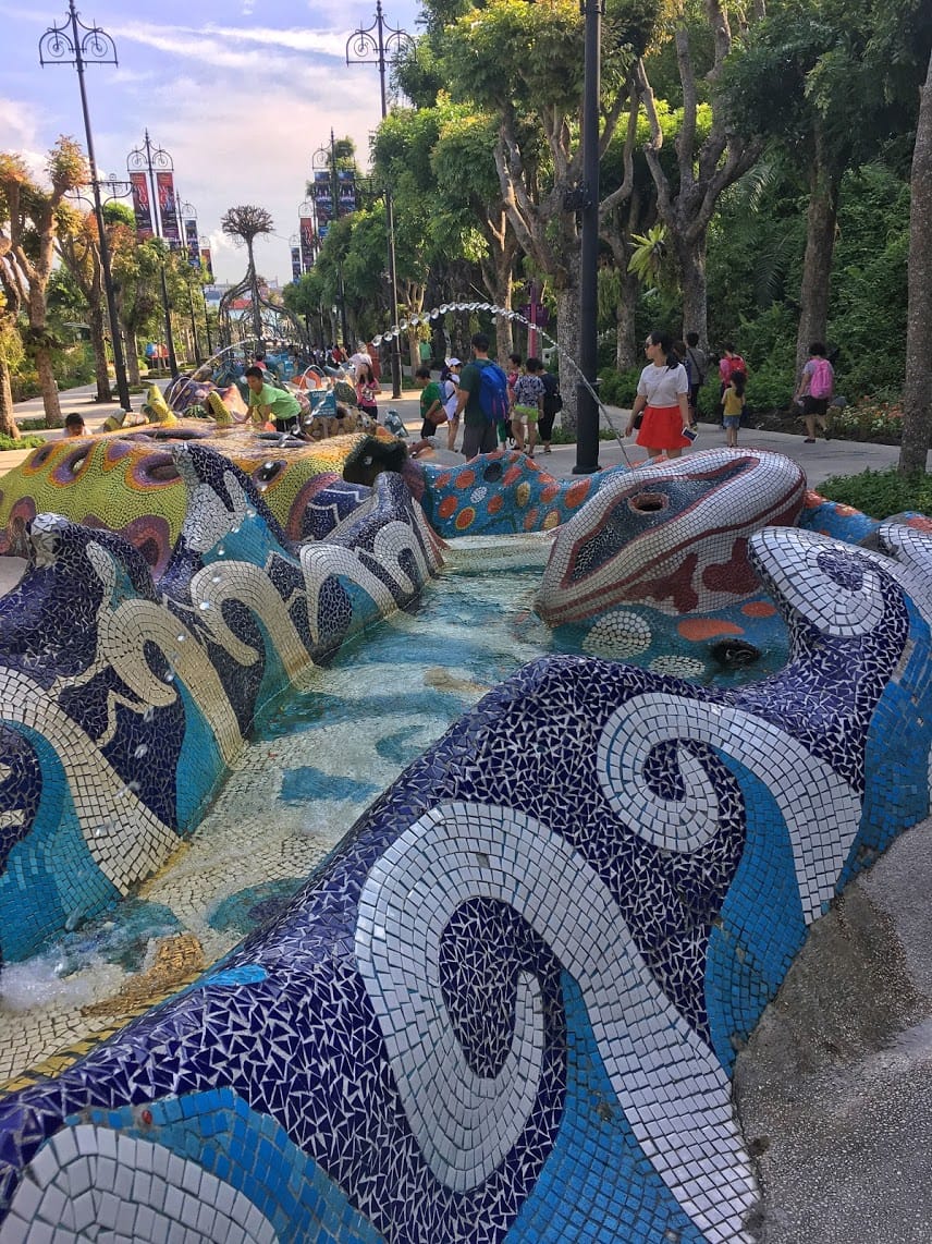 Gaudi inspired river and fountain meandering towards the water with kids playing and trees in the background