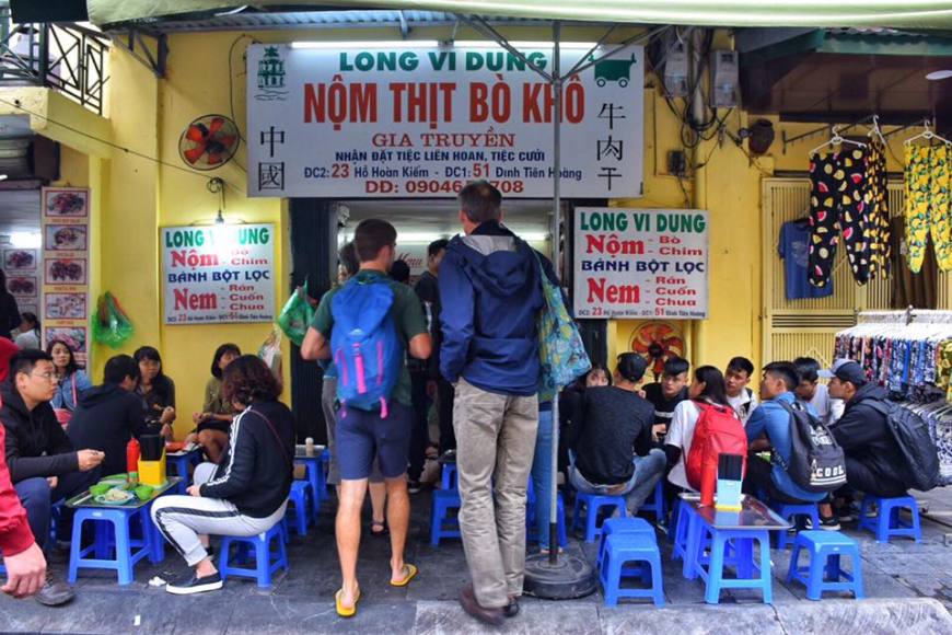 Two westerners walking into a restaurant in Hanoi where all seating is on ankle-high, blue stools