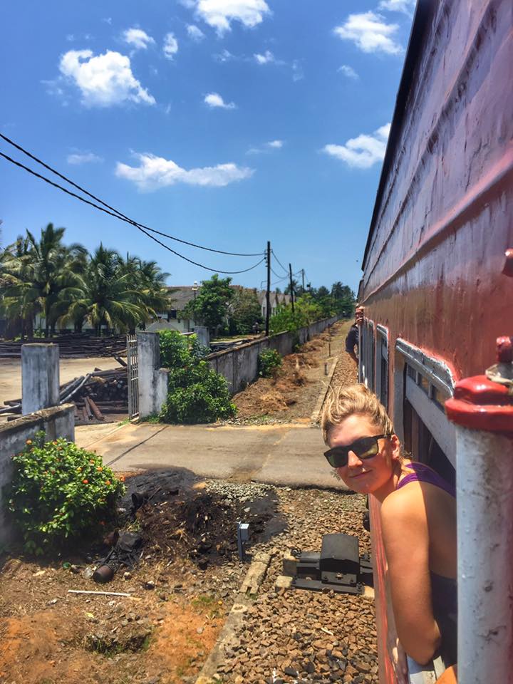 Blond haired woman with her head out the window of a train on a sunny day in Sri Lanka