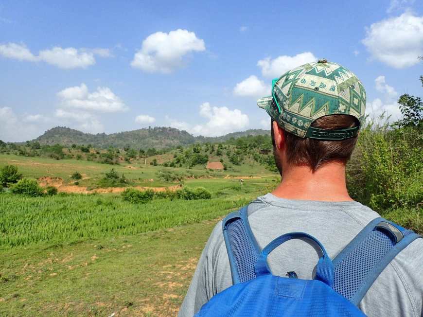Travel blogger Tj looking out over green fields and hills under a blue sky on our first day of trekking