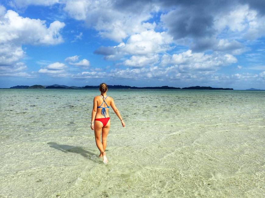 Woman in a red and blue bikini walking across a partially exposed sandbar in the middle of the ocean close to Port Barton, Philippines