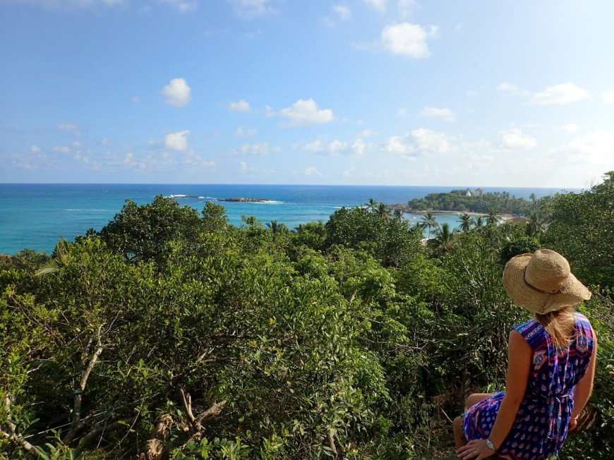 Viewpoint with a beautiful view of unawatuna beach over a tropical green forest with a woman in a sun