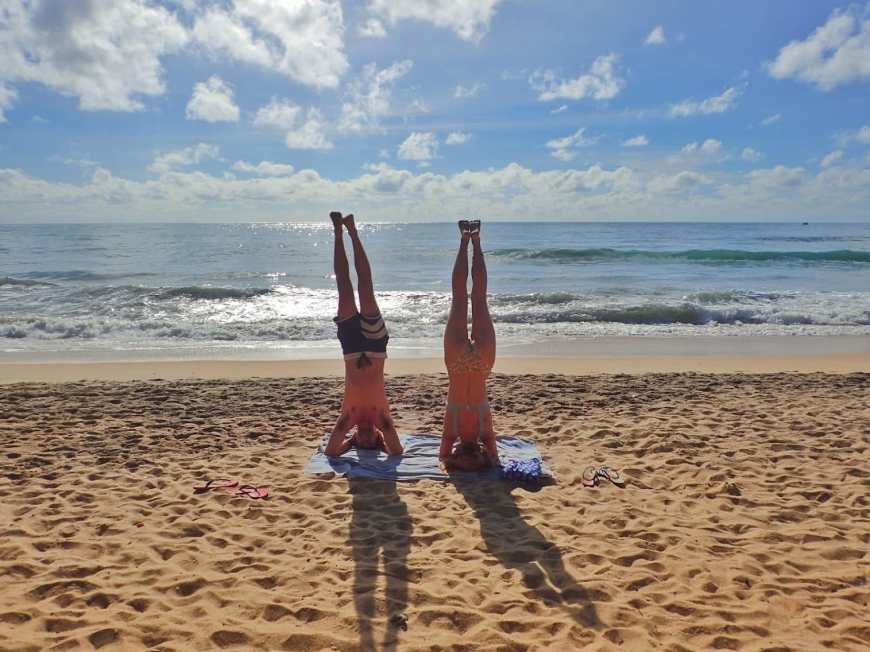Travel and adventure blogging couple doing headstands together on the sandy beach in the early morning