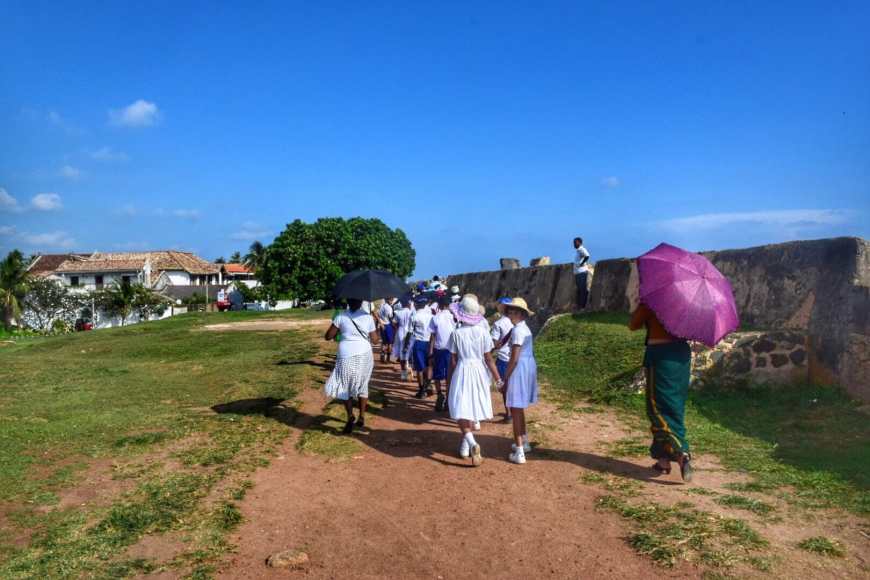 Group of Sri Lankan students in white dresses walking along the fort wall in Galle, Sri Lanka at the end of the school day