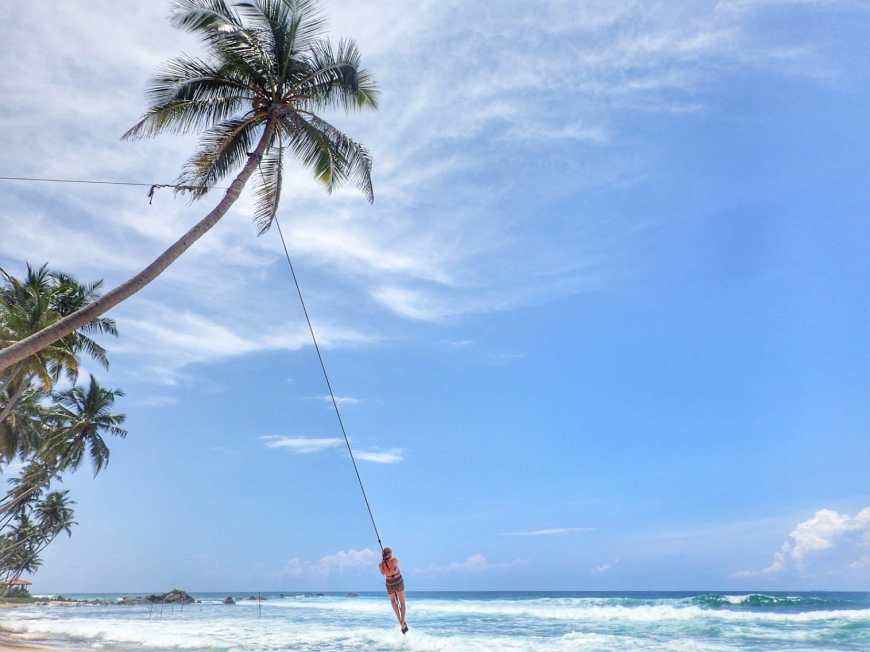 Woman swinging away above the ocean on a palm tree rope swing