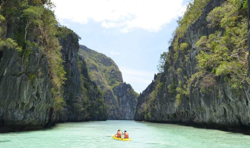 Two people kayaking in a yellow kayak down a waterway in El Nido, Palawan as rock crags jut out of the water