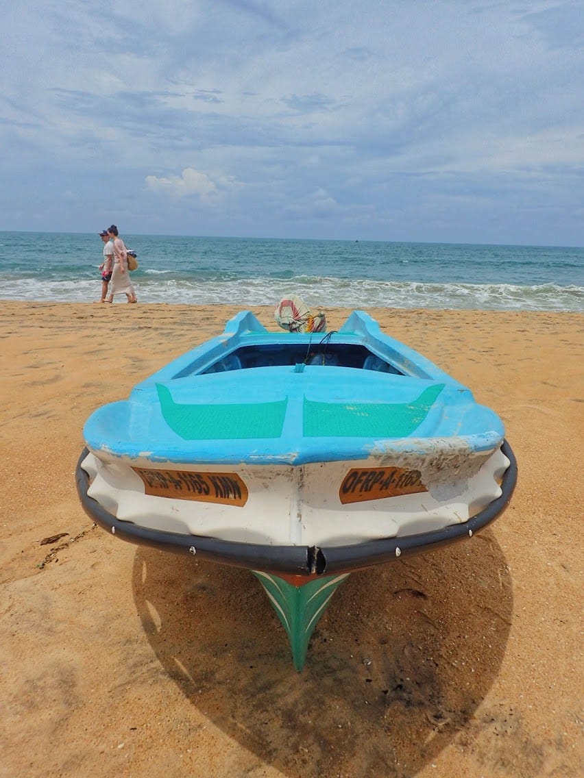 Traditional Sri Lankan bright blue fishing boat on the sand at the beach with a couple walking behind in the distance