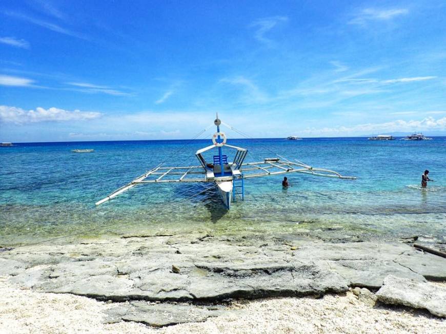 Filipino double outrigger crafts boat, called banca, floating just off the beach on a bright blue sea under the sun